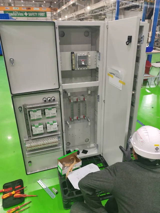 Open electrical cabinet with a technician inspecting components